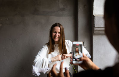 Two young women take photos and videos of each other on smartphone on a terrace