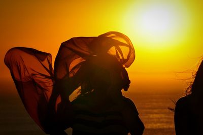 Woman silhouette waving fabric against sea during sunset