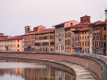 Arch bridge over river by buildings against sky