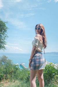 Portrait of young woman wearing sunglasses while standing by sea against sky