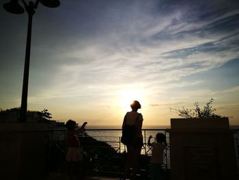 Silhouette people standing on beach against sky during sunset