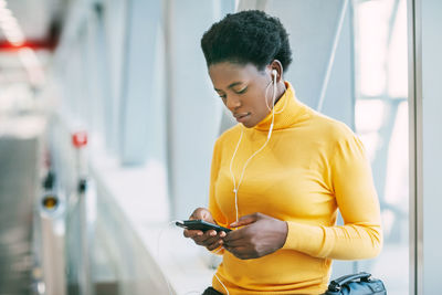 A young african woman listens to music with headphones, writes messages to friends and colleagues