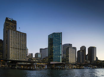 Modern buildings by river against clear sky