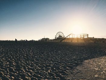 Ferris wheel on beach against clear sky during sunset