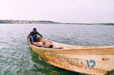 Man sitting on boat in sea against sky