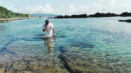 Full length of shirtless man in sea against sky