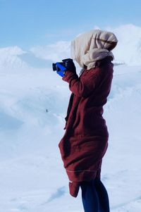 Side view of woman photographing on snowcapped mountain