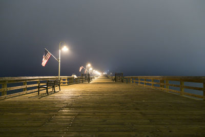 Illuminated footpath by pier against sky at night