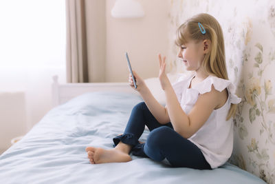 Full length of girl sitting on bed at home