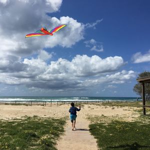 Rear view of boy flying over beach against sky