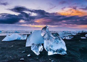 Icebergs on black sand at jokulsarlon lake against sky at sunrise