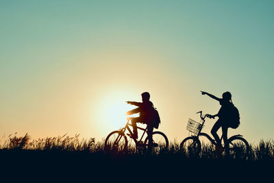 Silhouette of children with bicycle against clear sky