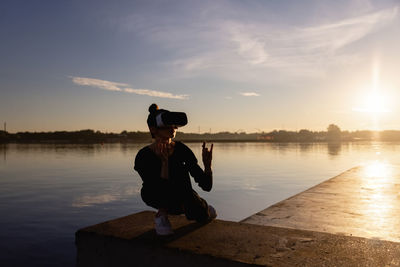 Rear view of woman standing by lake against sky during sunset