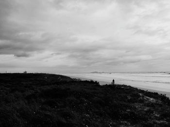 Silhouette person standing on shore by sea against sky