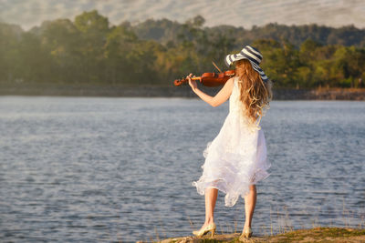 Rear view of woman playing violin by lake