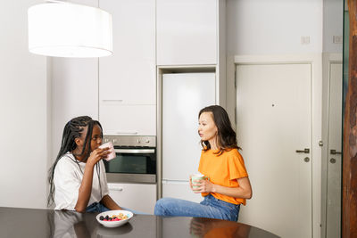 Young friends holding coffee cup while sitting at kitchen