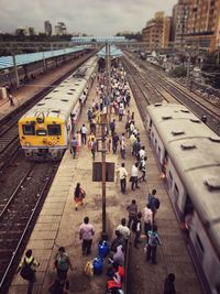 People on railroad station platform in city against sky