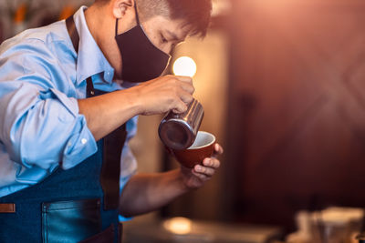 Man wearing mask while preparing coffee in cafe