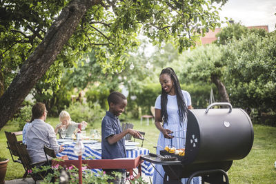 Mother and son preparing food on barbecue grill in yard during weekend party