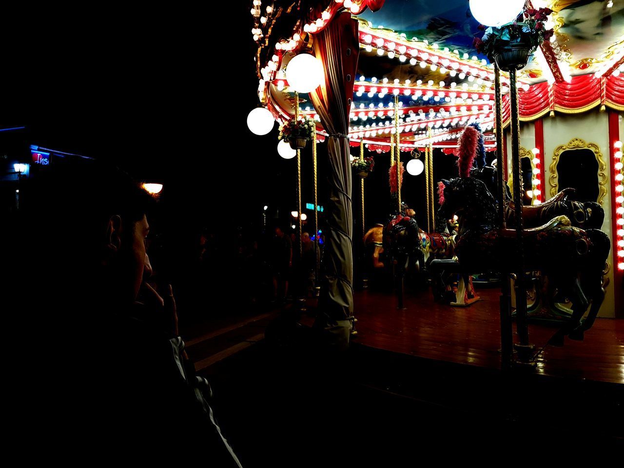 REAR VIEW OF PEOPLE AT ILLUMINATED AMUSEMENT PARK