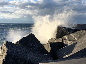 Waves splashing on rocks at shore against sky