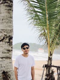 Portrait of man standing by coconut tree on the beach