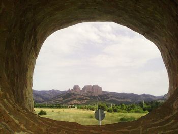View of field against sky seen through cave