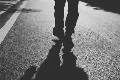 Low section of silhouette woman walking on road