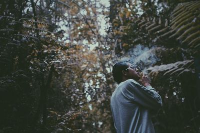 Low angel view of man smoking cigarette while standing against plants