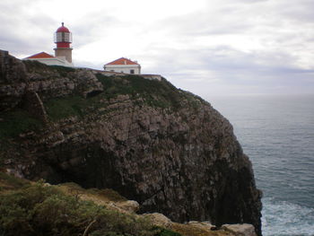 Lighthouse on cliff by sea against sky