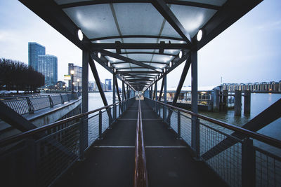 Footbridge over river against sky at dusk