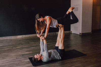 High angle side view of happy young barefooted couple in activewear looking at each other and smiling while doing balance exercise standing in front plank position on floor in contemporary studio