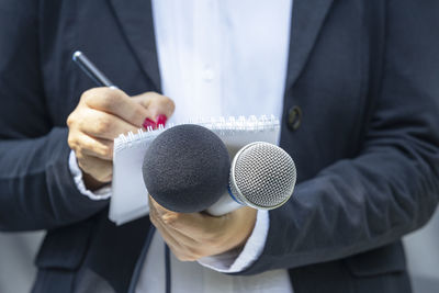 Female reporter at news conference or media event, writing notes, holding microphone