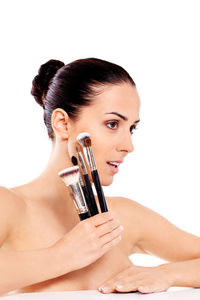 Close-up of shirtless female model holding make-up brushes against white background