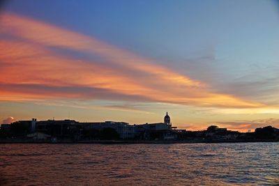 Silhouette buildings by sea against sky during sunset