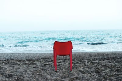 Red chair on beach against clear sky