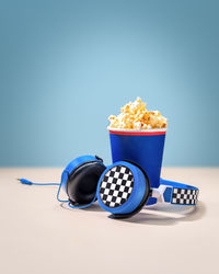 Composition with disposable cup with popcorn and headphones on a pink-blue background