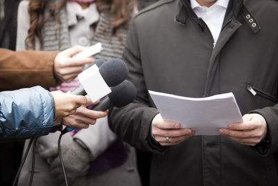 Cropped hands of reporters taking interview of man with document