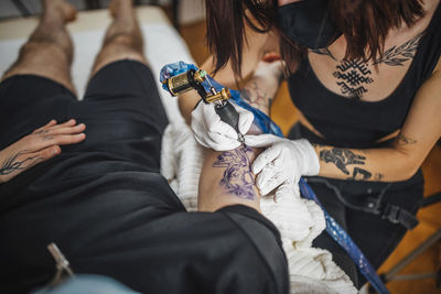 Top view of female tattoo master tattooing mans arm in a studio