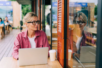 Business woman in glasses sitting at a table in a cafe uses a laptop for remote work.