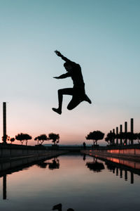 Silhouette man jumping over lake against sky during sunset