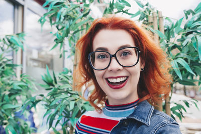 Portrait of smiling redhead young woman against plant