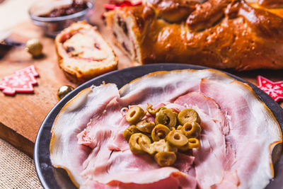 Slices of olives on ham in plate over table