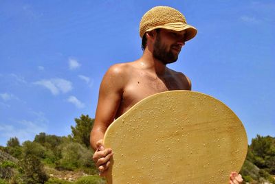 Full length of shirtless young man against sky on sunny day