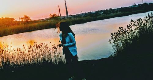 Man standing by lake against sky during sunset