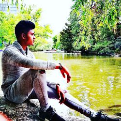 Side view of young man sitting by lake