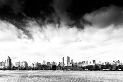 City at waterfront against cloudy sky