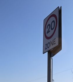 Low angle view of road sign against clear blue sky