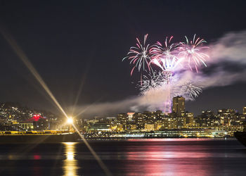 Firework display over illuminated city against sky at night