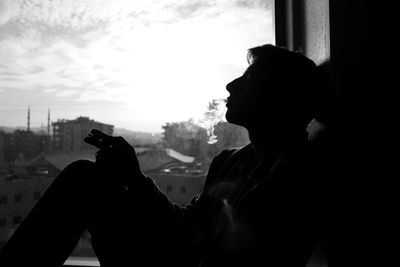 Side view of silhouette man smoking while sitting by window